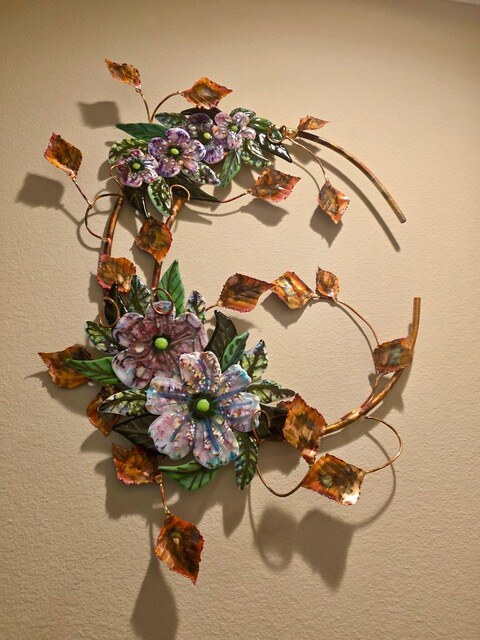 Wall sculpture of two copper circles carrying enameled glass flowers in purple and blue with copper leaves.