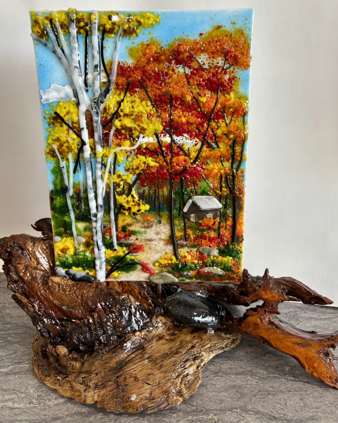 A fused-glass panel of white birch trees among orange and gold fall foliage, in a natural wood stand.