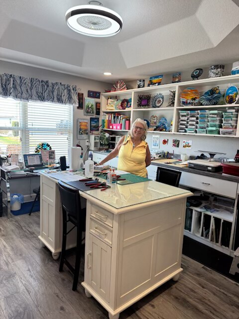 Annie standing in her home studio in The Villages, Florida, surrounded by shelves of fused-glass pieces.
