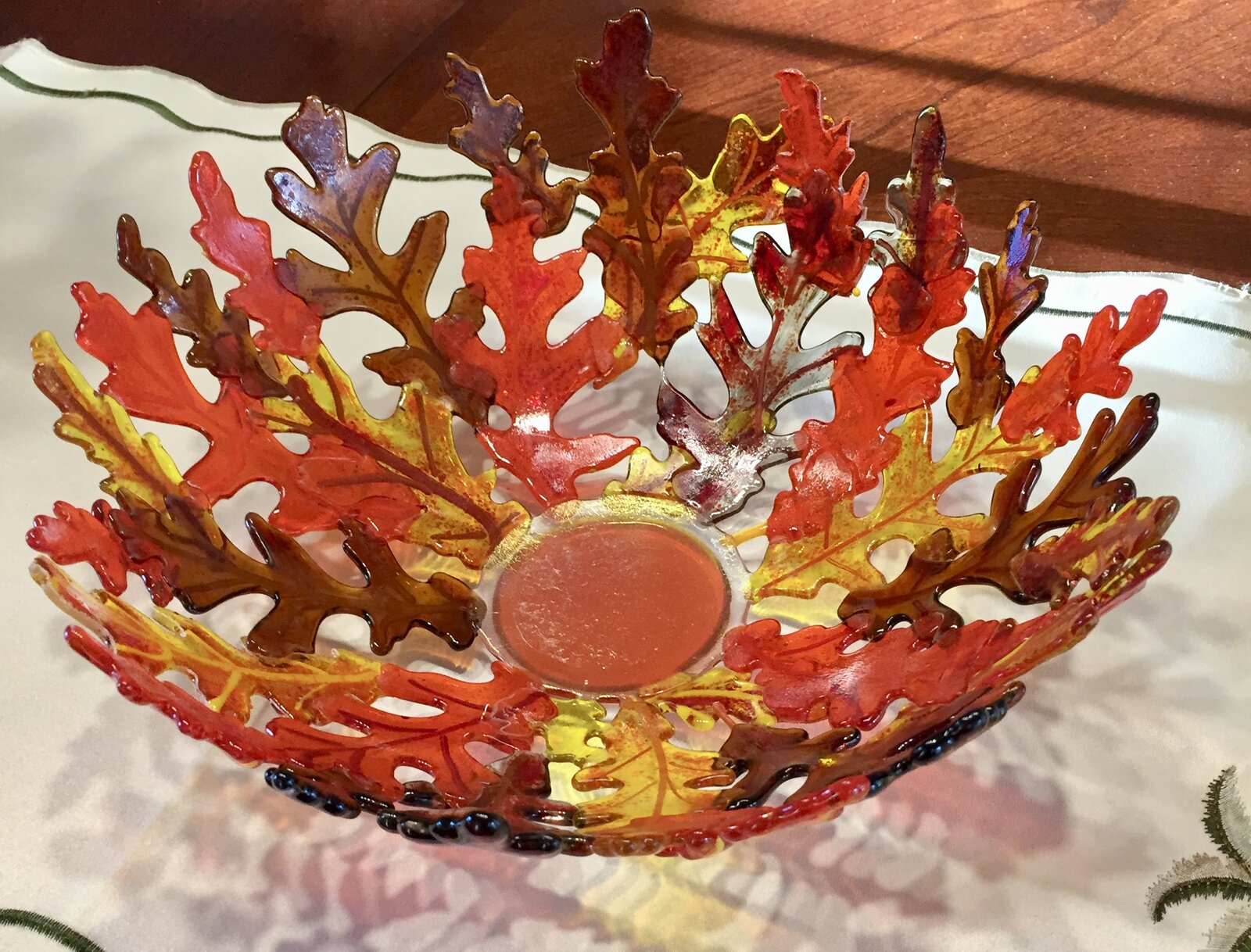 A fused-glass bowl built from overlapping red, orange, and amber oak leaves.