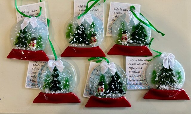 Snow Globe: fused-glass snow-globe ornaments with evergreens and a tiny snowman under falling snow, on a red base.