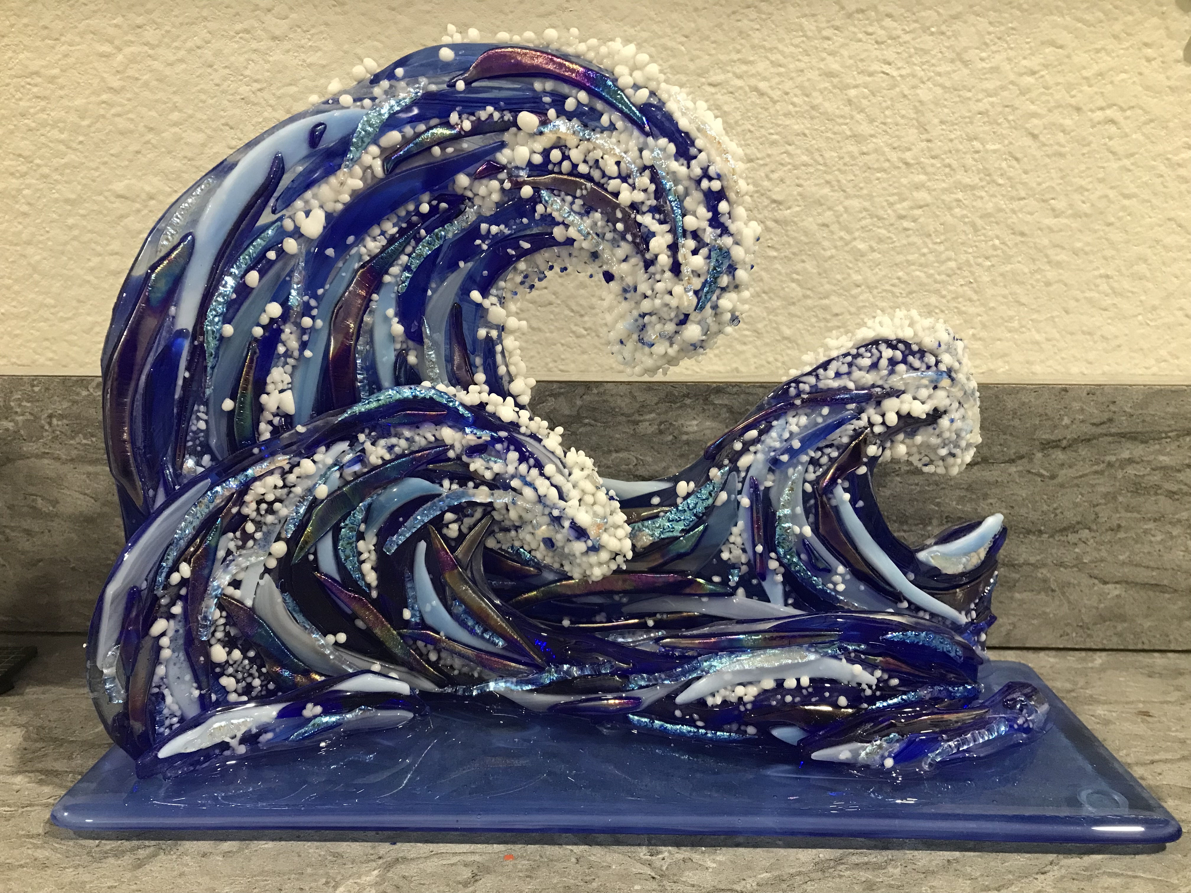 A 3D cobalt-blue fused-glass wave sculpture standing on a base, by Annie Dotzauer.